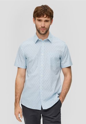 Chemise à manches courtes en bleu clair avec de petits motifs géométriques noirs, col classique et poche poitrine. Texture de tissu lisse.