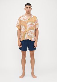 Camiseta de manga corta con estampado de tie-dye en patrones de naranja, amarillo y rosa, combinada con pantalones cortos de algodón azul marino. Tejido ligero, corte relajado.