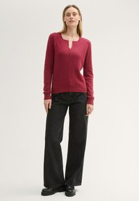 Fitted deep red sweater with long sleeves and a V-shaped neckline, paired with black wide-leg denim pants and chunky black shoes.