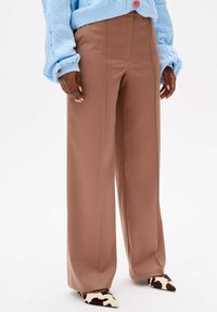 Bruine wijde pantalon met een soepele textuur en voorkreuken, gecombineerd met gestreepte puntige schoenen en een lichtblauwe gebreide trui.