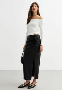 Vit off-shoulder topp med långa ärmar, kombinerad med en svart lädermaxikjol med rynkning och en sidöppning. Svarta platta skor fulländar looken.