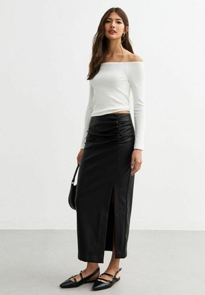 Witte off-the-shoulder top met lange mouwen, gecombineerd met een zwarte leren maxi rok met ruches en een zijsplit. Zwarte platte schoenen maken de look compleet.