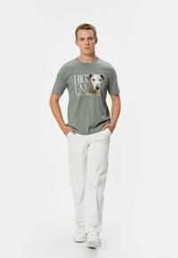 Camiseta gris con un gráfico de perro y texto, combinada con pantalones cargo blancos. El conjunto incluye zapatillas blancas y tiene un ajuste casual.