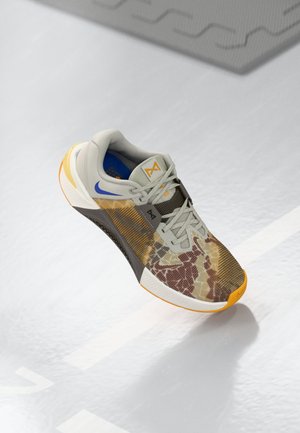 Athletic shoe featuring a gray upper with a multicolored camouflage pattern, orange accents, textured sole, and a padded collar for comfort.