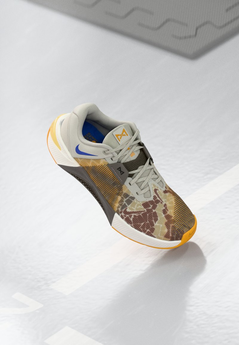 Athletic shoe featuring a gray upper with a multicolored camouflage pattern, orange accents, textured sole, and a padded collar for comfort.