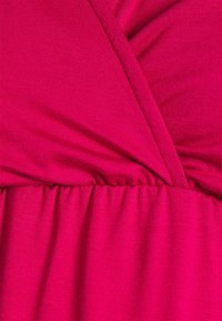 Detailní záběr jasně růžové látky se shrnovaným elastickým švem a překrývajícími se švy.