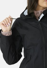 Giacca nera impermeabile con colletto alto, cappuccio regolabile e tasche con zip. Presenta una texture liscia e una vestibilità su misura.