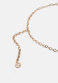 Zlata verižica z ovalnimi členkami in okroglo obesek na koncu, ki prikazuje cvetni izrez. Gladka tekstura.