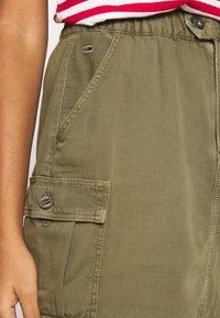 Olivgrön cargoskjol med sidoficka, knapprad och elastisk midja. Strukturerad tyg med synliga sömsdetaljer.
