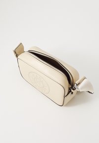 Borsa a tracolla in pelle beige con chiusura a zip, forma arrotondata, design goffrato sottile e tracolla in tessuto con dettagli in metallo.