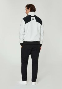 Herrbomberjacka i vitt med svarta detaljer, med hög krage, elastiska manschetter och logotypdetalj på baksidan. Matchar med svarta byxor.