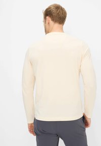 Langärmeliges hellbeiges Hemd mit rundem Ausschnitt, hergestellt aus weichem Stoff. Verfügt über eine normale Passform und eine glatte Textur.