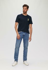 Granatowa koszulka bawełniana z krótkimi rękawami, z małym żółtym wzorem kwiatu na lewej piersi. Połączona z jasnoniebieskimi dżinsami i białymi trampkami.