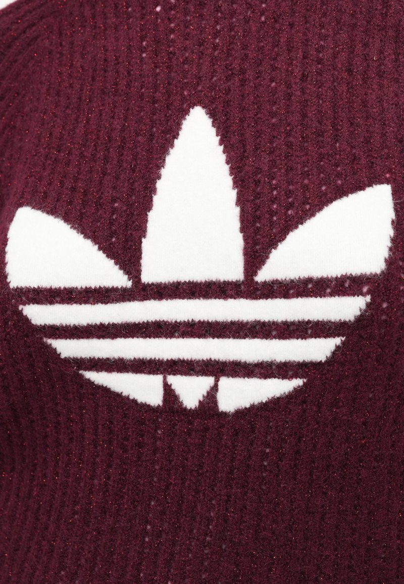 Burgunderfarbener Strickstoff mit einem großen weißen Adidas-Logo. Das Design umfasst drei Streifen und eine blattähnliche Form, mit einer strukturierten Oberfläche.