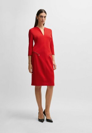 Red fitted dress made of textured fabric, featuring a deep V-neckline, three-quarter sleeves, and two zippered pockets at the front.