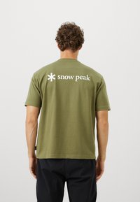 Olivgrünes T-Shirt mit kurzen Ärmeln, das auf der Rückseite ein weißes "Snow Peak"-Logo zeigt. Hergestellt aus weichem, leichtem Stoff mit lässiger Passform.