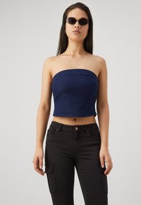 Džínový bezramínkový crop top v tmavě modré barvě; přiléhavý design, hladká textura. Spárováno s černými cargo kalhotami s bočními kapsami a zapínáním na knoflík.