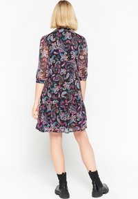 Svart klänning med livfull paisleymönster i lila, turkos och rosa. Genomskinliga 3/4-långa ärmar, över knä-längd, tillsammans med ankelskor.