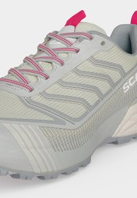 Αθλητικό παπούτσι ανοιχτού γκρι χρώματος με κορδόνια σε ροζ απόχρωση, επάνω μέρος από διαπνέον πλέγμα, υφή στην σόλα και καλουπωμένες πλευρικές λεπτομέρειες για υποστήριξη και κράτημα.