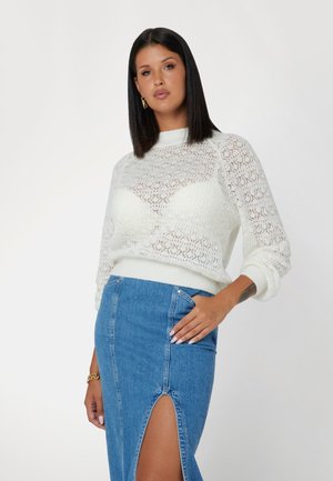 Maglione bianco a maglia con un motivo in pizzo, con orlo a coste. Abbinato a una gonna di jeans a vita alta con uno spacco laterale e dettagli con tasche.