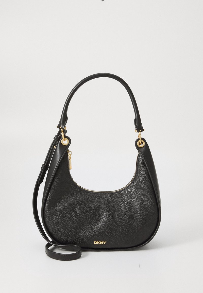 Sac à main en cuir noir DKNY avec ferrures dorées, poignée supérieure incurvée et bandoulière amovible sur fond clair uni.