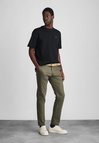 T-shirt in cotone nero abbinato a pantaloni kaki. L'outfit presenta maniche arrotolate, una cintura beige e sneakers bianchi. Design semplice.
