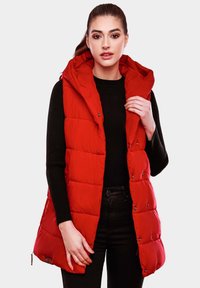 Red puffer vest with a hood, featuring quilted sections, snap buttons, and a long design, worn over a black ribbed sweater.