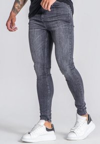 Vaqueros ajustados de mezclilla gris oscuro con un ligero desvanecimiento y detalles de costura, combinados con zapatillas blancas con acentos grises.