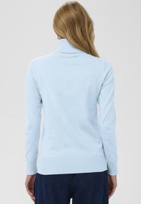 Ljust blå långärmad tröja med hög halsdesign, ribbade ärmmuddar och fåll, med en jämn, mjuk textur. Inga synliga mönster.