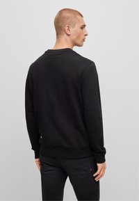 Felpa nera con collo a giro e maniche lunghe, caratterizzata da una superficie liscia e polsini e orlo a coste. Design semplice e classico.