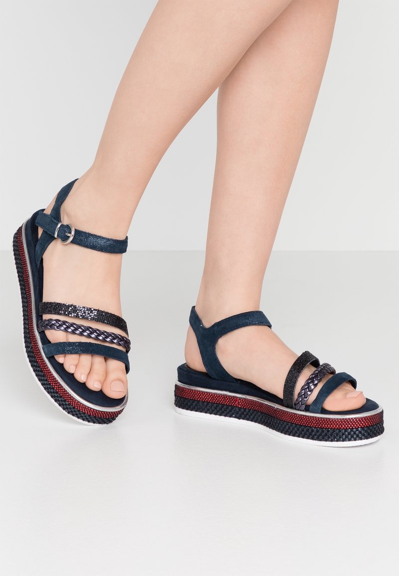 Sandales compensées en suède bleu marine avec trois lanières, dont un détail tressé. La semelle texturée dispose de surpiqûres rouges et noires.