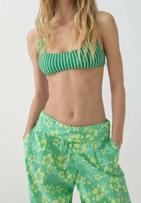 Zielony bikini top w paski z teksturowanym wzorem, w połączeniu z luźnymi zielonymi spodniami w kwiatowy wzór z żółtymi kwiatami i sznurkiem w talii.
