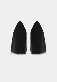 Svart høye hæler med spiss tå og bred blokkhelt, med en glatt tekstur og minimalistisk design. Bakfra vist.
