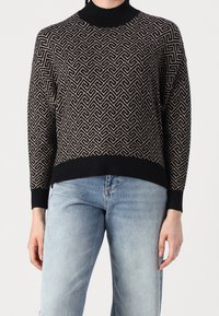 Pull noir et beige à motif avec un col montant, une coupe ample et des poignets côtelés. Le design présente un motif géométrique complexe.