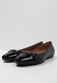 Czarne lakierowane baletki ze zaokrąglonym noskiem, o eleganckim designie i dekoracyjną kokardką na wierzchu. Płaska podeszwa.