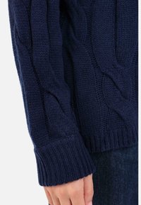 Marineblauer, gestrickter Pullover mit Zopfmuster, gerippten Bündchen und Saum, der eine weiche Textur und eine dicke Garnverarbeitung aufweist.