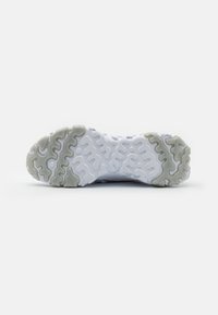 Suela de zapato deportivo blanco con un patrón ondulado y texturizado; secciones en gris claro y blanco. Diseñada para tracción y durabilidad.