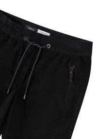 Zwarte broek met een elastische tailleband, trekkoordsluiting en zilveren ogen. Bevat een zijzak met rits en een gestructureerde stof.
