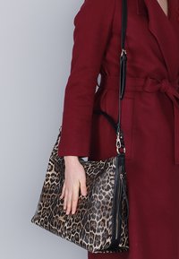 Handväska i leopardmönster med svarta accenter. Har dragkedjestängning, texturerat material och en lång justerbar axelrem.