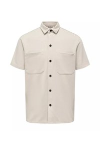 Camisa beige de manga corta con cuello abotonado, que cuenta con dos bolsillos frontales y botones negros en una tela suave y texturizada.