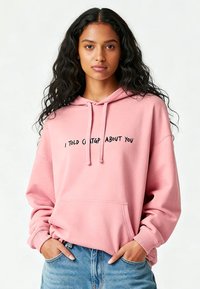 Roze hoodie met trekkoord, zak aan de voorkant en zwarte tekst met de woorden 'IK HEB CHATGPT OVER JOU VERTELD.' De stof lijkt zacht met een ontspannen pasvorm.