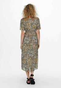 Robe maxi en imprimé léopard en tissu léger, dotée de manches courtes, d'une taille cintrée et d'une jupe fluide. Portée avec des sandales noires.