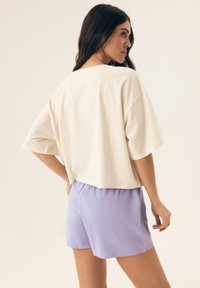 Biała krótka koszulka z krótkim rękawem w połączeniu z jasnofioletowymi szortami. Koszulka ma okrągły dekolt i luźny krój, wykonana z bawełny.