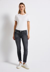 Harmaat slim-fit farkut, joissa on käännettävät lahkeet, yhdistettyinä yksinkertaiseen valkoiseen t-paitaan ja valkoisiin lenkkareihin. Luonnollinen kangas ja yksinkertaiset muotoiluelementit.