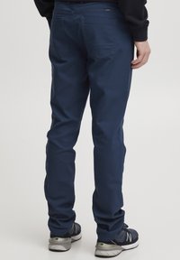 Mornarji modri hlače iz mešanice bombaža, ki imajo ozko prileganje, zadnje žepe s ukrivljenim šivom in gladko teksturo. V kombinaciji s športnimi čevlji.