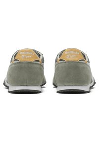 Zelené semišové sportovní boty s bílými a žlutými akcenty, s texturovaným podpatkem a kontrastní černou gumovou podrážkou.