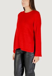 Maglione rosso morbido con scollatura rotonda e maniche lunghe, abbinato a pantaloni in pelle nera. Il maglione ha una vestibilità comoda e leggere fessure laterali.