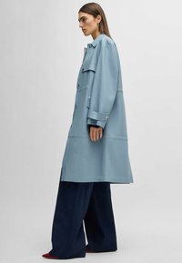 Light blue, oversized trench coat made of smooth material with a button front, large pockets, and contrasting navy wide-leg pants.