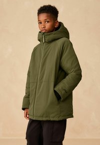 Olivgrüne gepolsterte Jacke mit Reißverschluss und großer Kapuze; sie hat einen lockeren Schnitt, große Seitentaschen und elastische Bündchen.