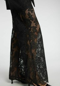 Mustat pitsihousut, joissa on kukkakuosi, rento istuvuus ja läpikuultava rakenne, koristeena aaltoilevat reunat ja hienovarainen läpinäkyvyys.